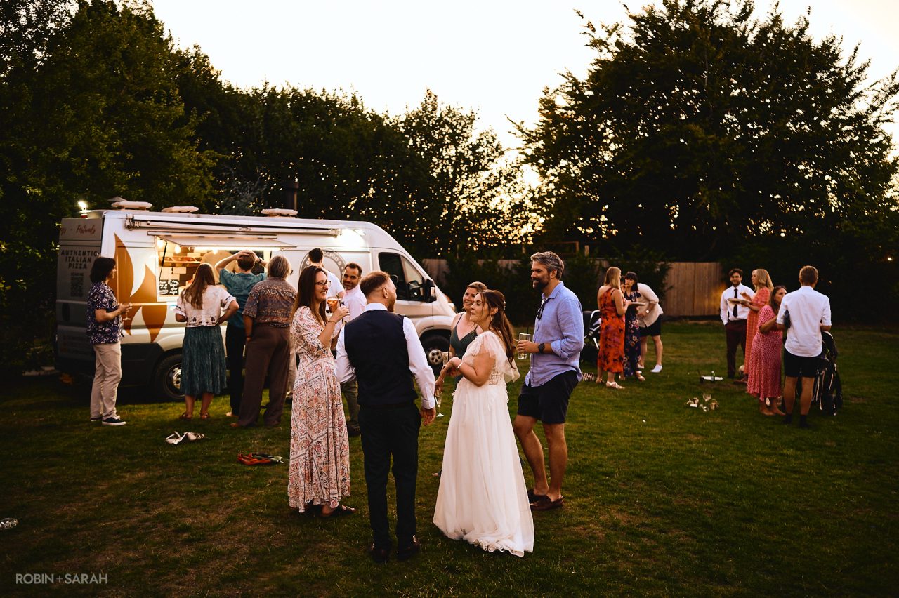 Bride, groom and friends relaxing with drinks and pizza in the gardens at Charingworth House