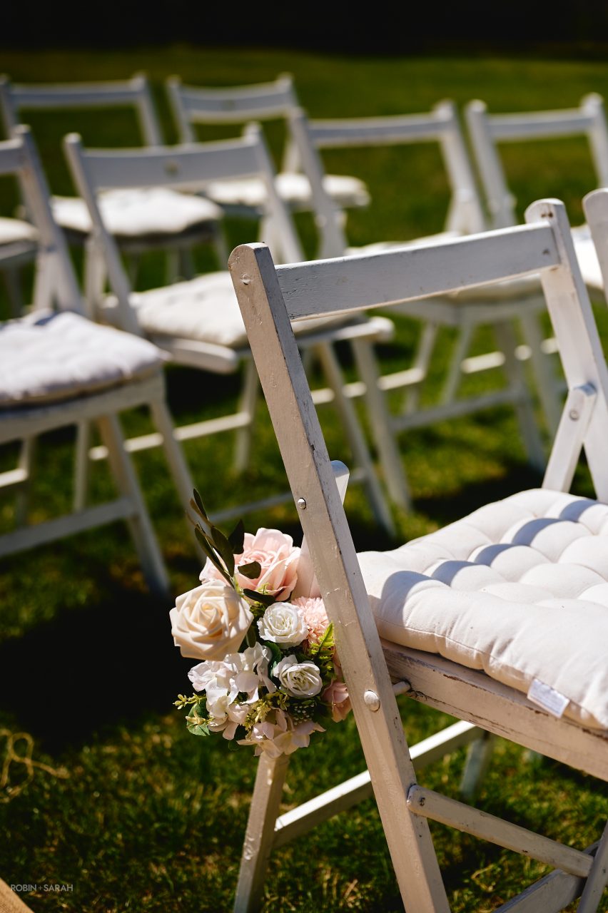 Wooden chairs set out for wedding ceremony with flowers tied to frames