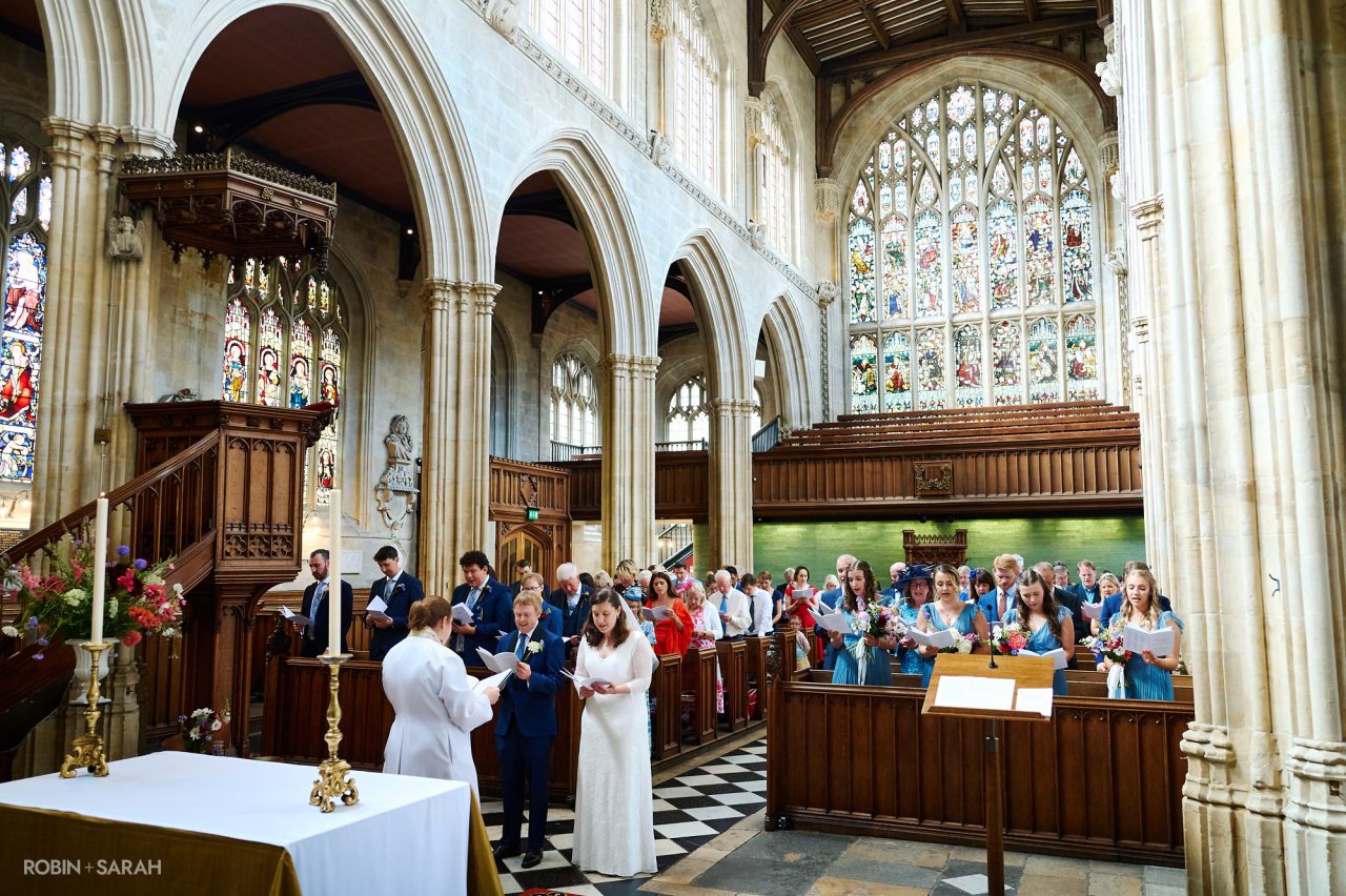 Bride, groom and congregation sing hymn during wedding service at University Church in Oxford