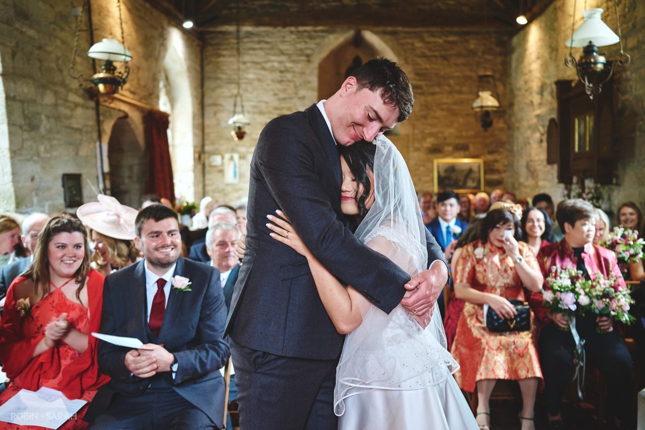 Groom hugs bride at end of wedding ceremony at St Nicolas Church, Dormston, near Worcester