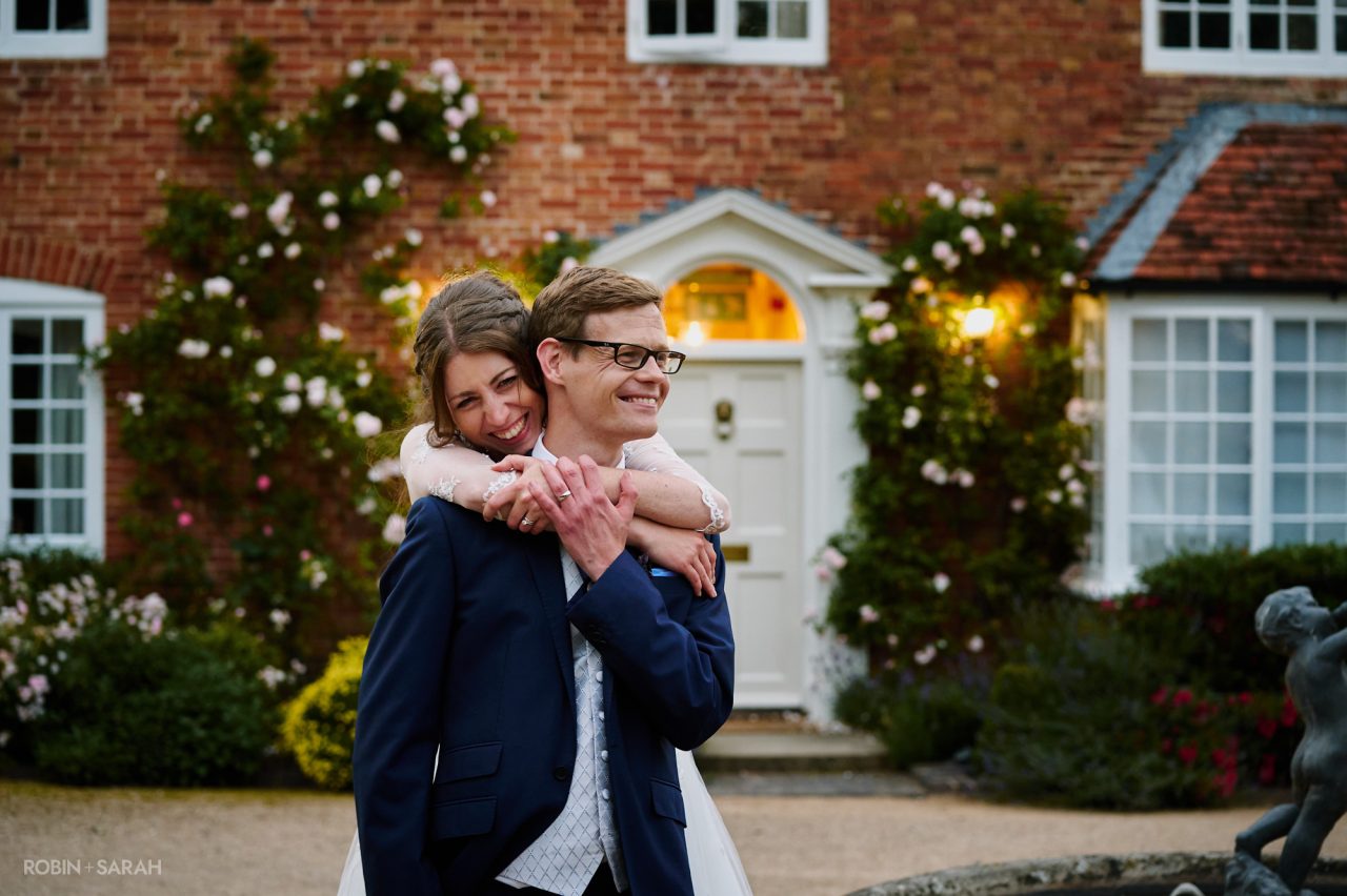 Bride wraps her arms around groom outside main house at Wethele Manor