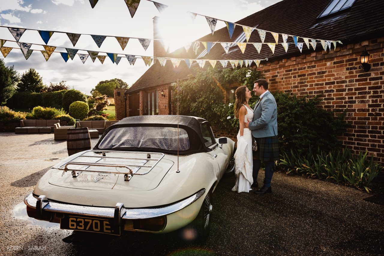 Bride and groom next to E-type Jaguar wedding car in courtyard at Wethele Manor