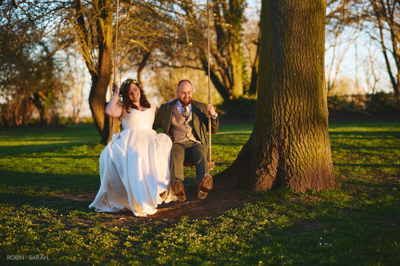 Bride and groom sitting on swing under tree with beautiful evening light at Wethele Manor