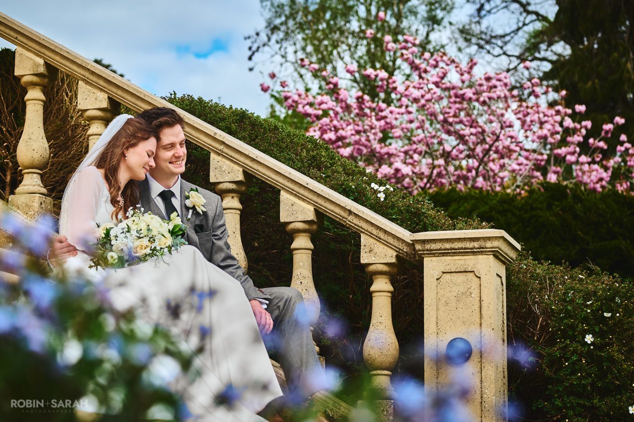 Bride and groom sitting on steps at Kilworth House with beautiful flowers in the foreground and pink blossom in the background