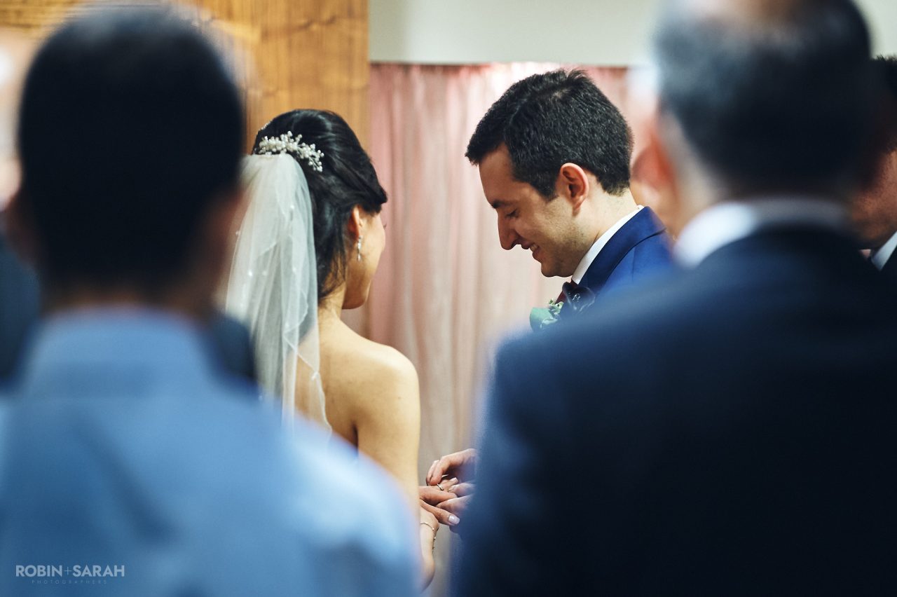 Groom place wedding ring on bride's finger during ceremony at Solihull Register Office