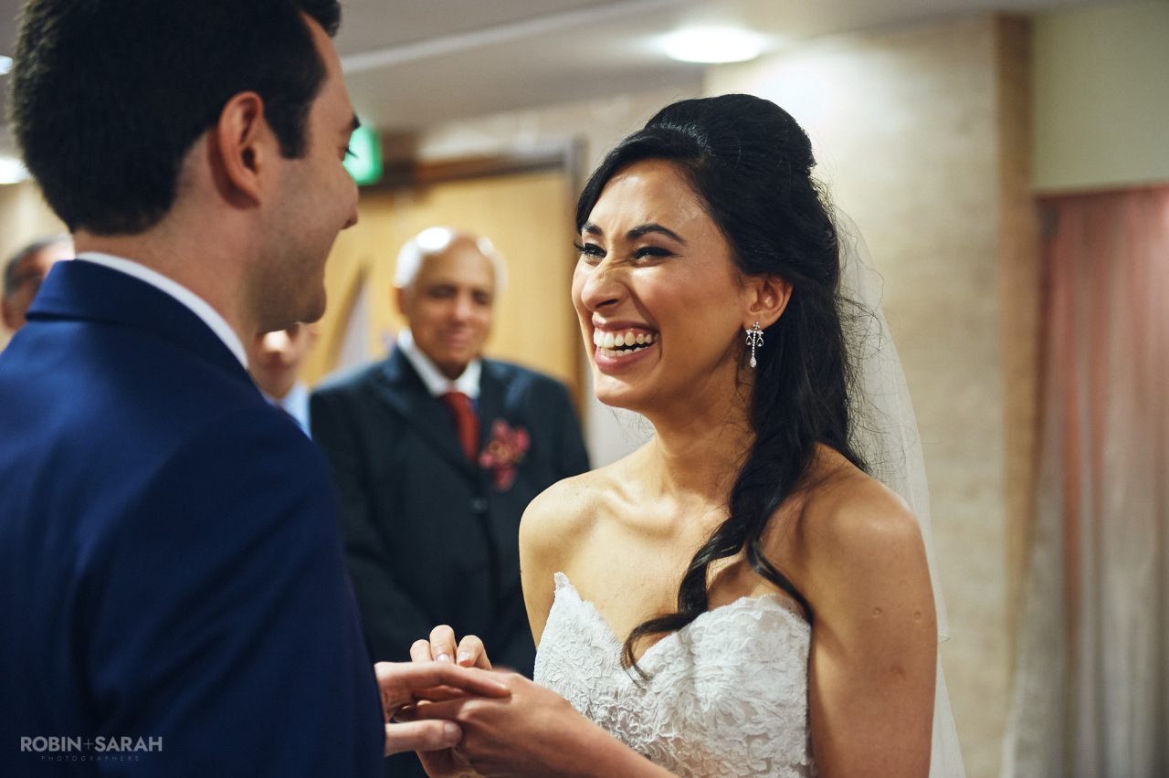 Bride laughing as she places wedding ring on groom's finger