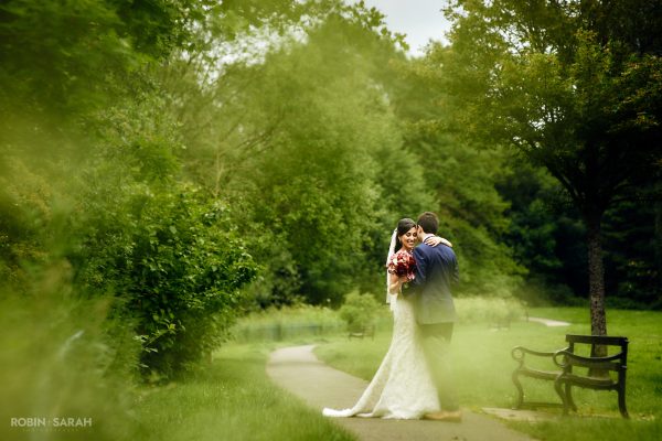 Bride hugs groom on pathway at Brueton Park, Solihull, with soft foliage surrounding them