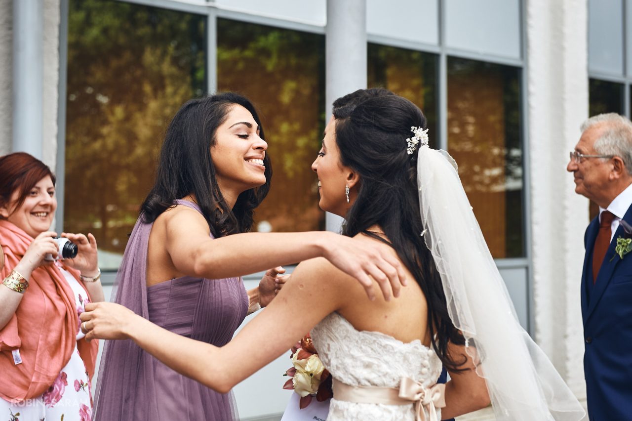 Bridesmaid hugs bride outside Solihull Register Office